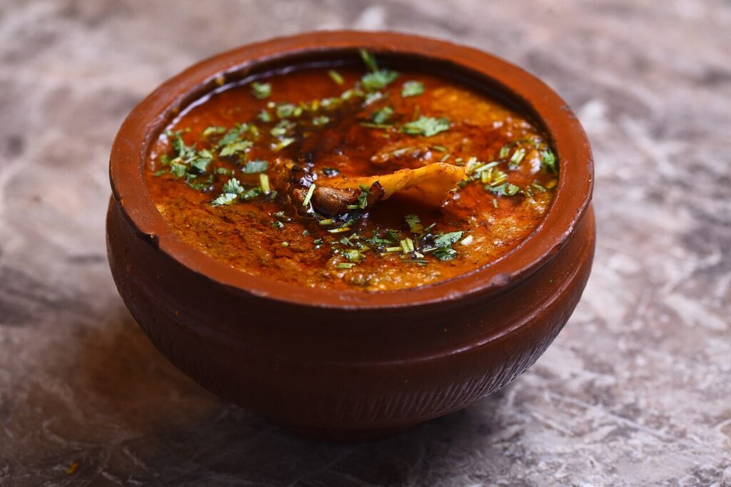 A clay pot of beef nihari garnished with ginger and chillies