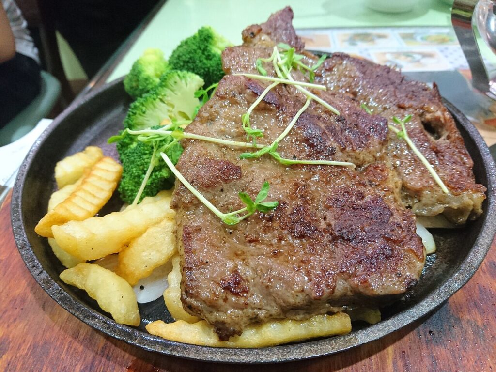 Beef steak with fries and greens on a sizzling plate