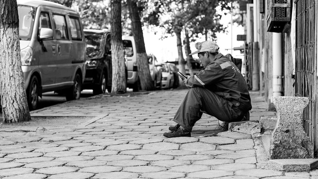A young man sitting on a pavement, absorbed in his phone